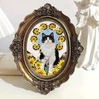 Decorative framed picture of a black and white cat among yellow flowers on a white surface.